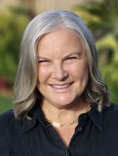 colour portrait image of female Katie Willey Director of Soulutions Consulting in blue shirt with grey hair and greenery background