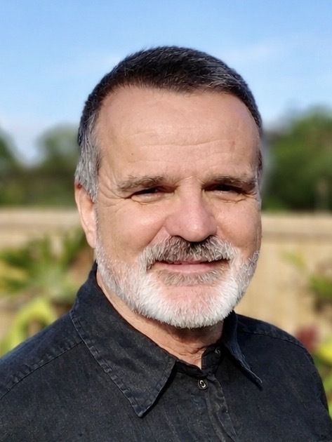 portrait image of male Malcolm Brown Director Soulutions Consulting with black shirt, dark hair and greenery background